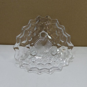 Puede incluir: Plato de servir de vidrio transparente con borde festoneado y un patrón geométrico texturizado. El centro presenta un diseño de estrella. El plato es transparente y está sobre una superficie blanca.