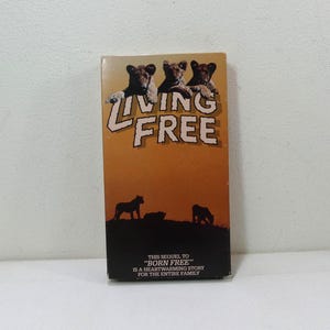 May include: A vintage VHS tape for the movie "Living Free." The cover features three lion cubs above the title in large, orange letters. The background is a sunset scene with silhouettes of lions. The text reads "This sequel to 'Born Free' is a heartwarming story for the entire family."