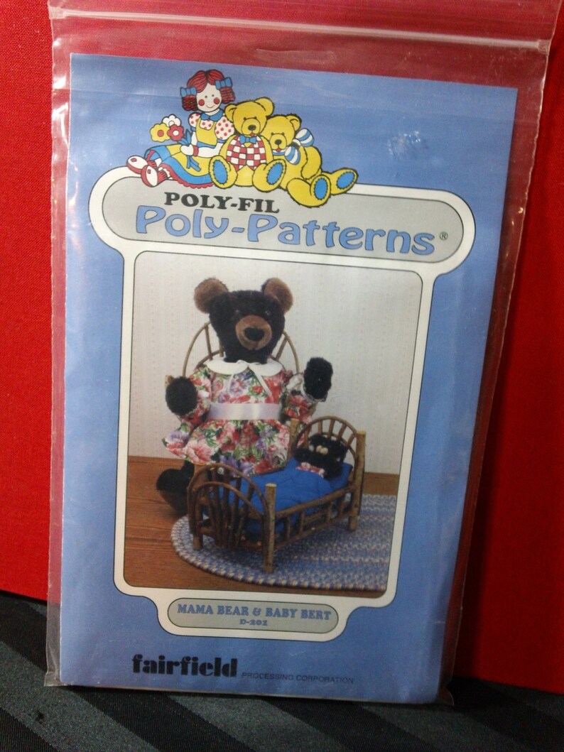 May include: A blue Poly-Fil Poly-Patterns package featuring a Mama Bear and Baby Bert design. The image shows a black bear wearing a floral dress and a baby bear in a wooden bed. The package also features illustrations of teddy bears.