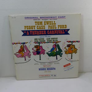 May include: A vintage vinyl record album cover for "A Thurber Carnival" featuring the original Broadway cast. The cover has colorful illustrations of carousel animals and text including the names of the cast and the title.