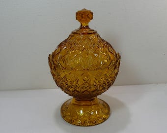 May include: A vintage amber glass candy dish with a lid. The dish has a round body with a pedestal base and a decorative diamond pattern.