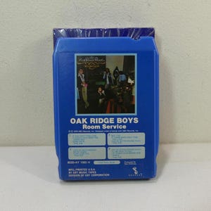 Puede incluir: Una cinta de 8 pistas azul del álbum "Room Service" de Oak Ridge Boys. La portada del álbum presenta una foto de la banda. La cinta tiene los títulos de las canciones enumerados en la parte delantera.