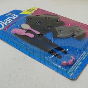 May include: A plastic package containing a black and white doll outfit, a pink comb, a pink hair clip, and a silver hand mirror. The package is labeled "Diana" and "Classic Fashion".