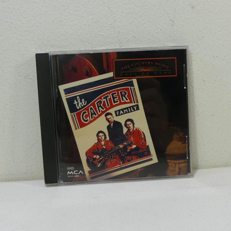 May include: A CD case featuring "The Carter Family" album cover. The cover art displays a vintage photograph of the musical group, with the text "The Country Music Hall of Fame" at the top. The CD case is in a clear plastic case.