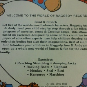 May include: A vintage record album cover featuring Raggedy Ann and Andy. The cover is yellow with a red heart shape in the center. The text on the cover reads "Welcome to the World of Raggedy Records!" and lists exercises for children, including "Reaching Stretching", "Jumping Jacks", "Rocking Boats", "Elephant", "Monkey", "Seal", "Bird", "Kangaroo", and "Marching".