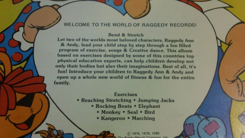 May include: A vintage record album cover featuring Raggedy Ann and Andy. The cover is yellow with a red heart shape in the center. The text on the cover reads "Welcome to the World of Raggedy Records!" and lists exercises for children, including "Reaching Stretching", "Jumping Jacks", "Rocking Boats", "Elephant", "Monkey", "Seal", "Bird", "Kangaroo", and "Marching".