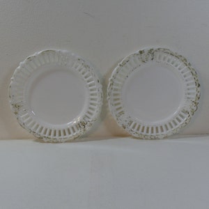 May include: Two white porcelain plates with a delicate openwork design and gold accents. The plates have a scalloped edge and a floral motif.