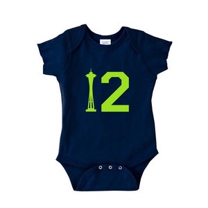 Peut inclure: Une grenouill&egrave;re b&eacute;b&eacute; bleu marine avec une silhouette verte de la Space Needle et le num&eacute;ro 12.