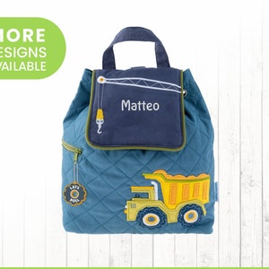 May include: A blue quilted backpack with a yellow dump truck design. The backpack has a flap with a navy blue pocket that says "Matteo" in white embroidery. The backpack has a zipper on the side and a small tag that says "Let's Roll".