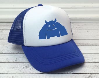 May include: A blue and white trucker hat with a blue monster graphic. The monster has two eyes, a mouth, and a tongue sticking out.