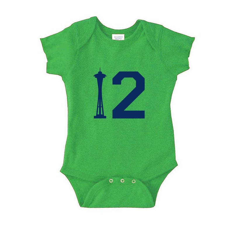 Peut inclure: Combinaison b&eacute;b&eacute; de couleur verte avec une silhouette bleue marine de la Space Needle et le chiffre 12.