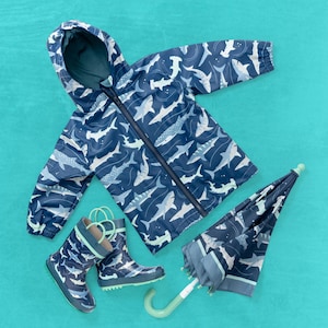 May include: A blue raincoat with a shark print, a pair of blue rain boots with a shark print, and a blue umbrella with a shark print.