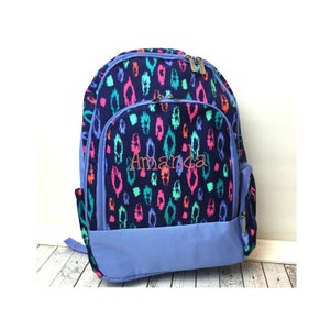 May include: A blue backpack with a colorful ikat pattern and the name "Amanda" embroidered on the front. The backpack has a blue zipper and a blue pocket on the side.