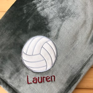 May include: A gray fleece blanket with a white volleyball and the name "Lauren" embroidered in red.