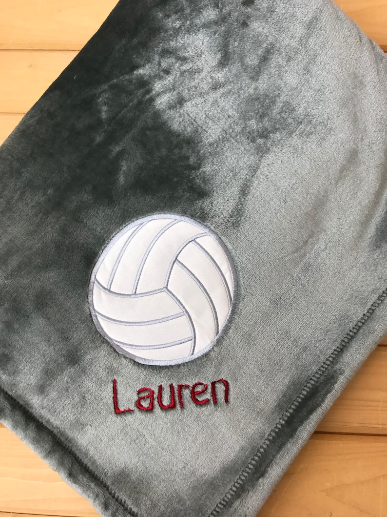 May include: A gray fleece blanket with a white volleyball and the name "Lauren" embroidered in red.