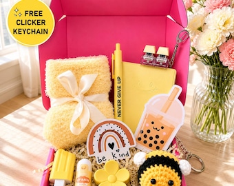 May include: A bright pink gift box containing a yellow fuzzy blanket with a white ribbon, a yellow notebook with a smiley face, a yellow pen labeled NEVER GIVE UP, a boba tea sticker, a rainbow sticker, a yellow popsicle eraser, lip balm, a flower, and a bee.