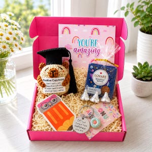 Pode incluir: Uma caixa de presente rosa contendo uma capivara de crochê com capelo preto, uma caixa de chá preto Lovaré Bergamot Truffle, um adesivo em formato de lápis, um chaveiro de donut com etiqueta e um cartão com a frase You're amazing.