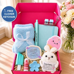 Op de afbeelding: Een felroze geschenkdoos met een paar lichtblauwe, pluizige sokken met een wit lint, een lichtblauw notitieboek met een pen met de tekst DREAM BIG, een gehaakt konijntje met een bordje, een ijsje en een lippenbalsem in de doos.