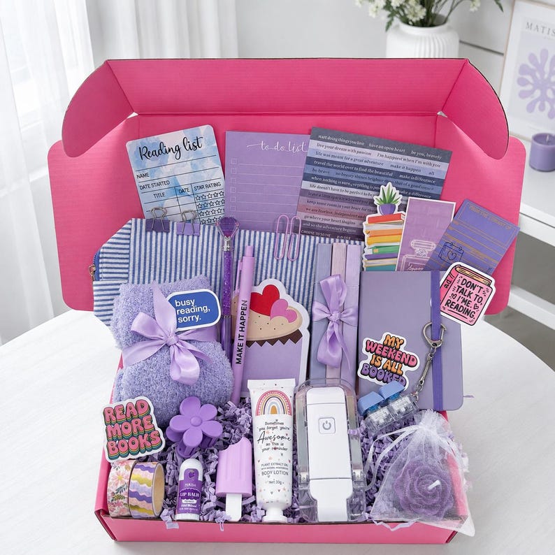 May include: A bright pink gift box filled with purple and blue themed items including a reading list card, a to-do list, a striped pencil case, a purple fuzzy blanket with a bow, a pen, a cupcake notepad, lotion, a book light, and stickers.