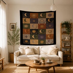 May include: A large, square tapestry with a black border, featuring a grid of celestial designs. Each square showcases a sun, moon, or star in shades of gold, orange, and purple against a dark background. The tapestry is hanging on a white wall.
