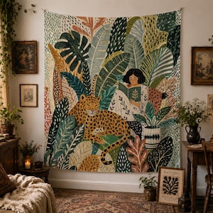 May include: A tapestry featuring a leopard amidst lush foliage, with a person reading a book. The design incorporates various shades of green, brown, and orange, creating a vibrant jungle scene. The tapestry is a decorative wall hanging.