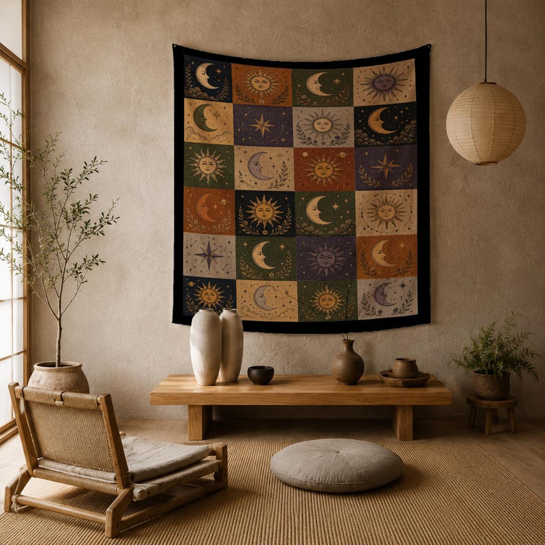 May include: A tapestry with a black border features a patchwork design of suns, moons, and stars in various colors. The squares are in shades of orange, green, purple, and beige. The tapestry is hanging on a neutral-colored wall.