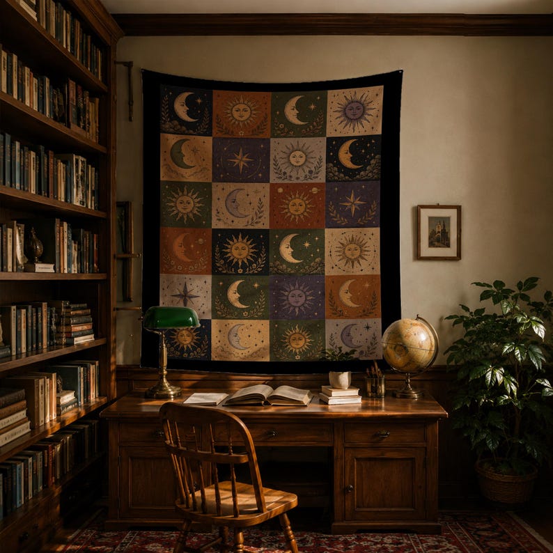 May include: A tapestry featuring a celestial design of moons and suns in a grid pattern hangs above a wooden desk. The desk is in a room with bookshelves and a globe. The tapestry has a black border and a variety of colors.