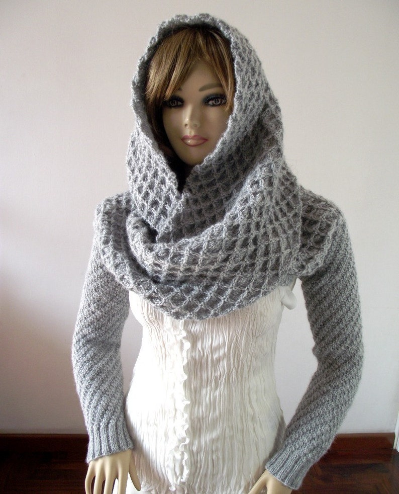 May include: Gray knitted cowl neck sweater with long sleeves and a hood. The sweater has a waffle stitch pattern.