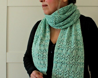 May include: A long, rectangular knit scarf in a light mint green color featuring an intricate, openwork lace pattern. The scarf is wrapped loosely around the neck, with two long ends hanging down the front, showcasing the detailed, airy texture.