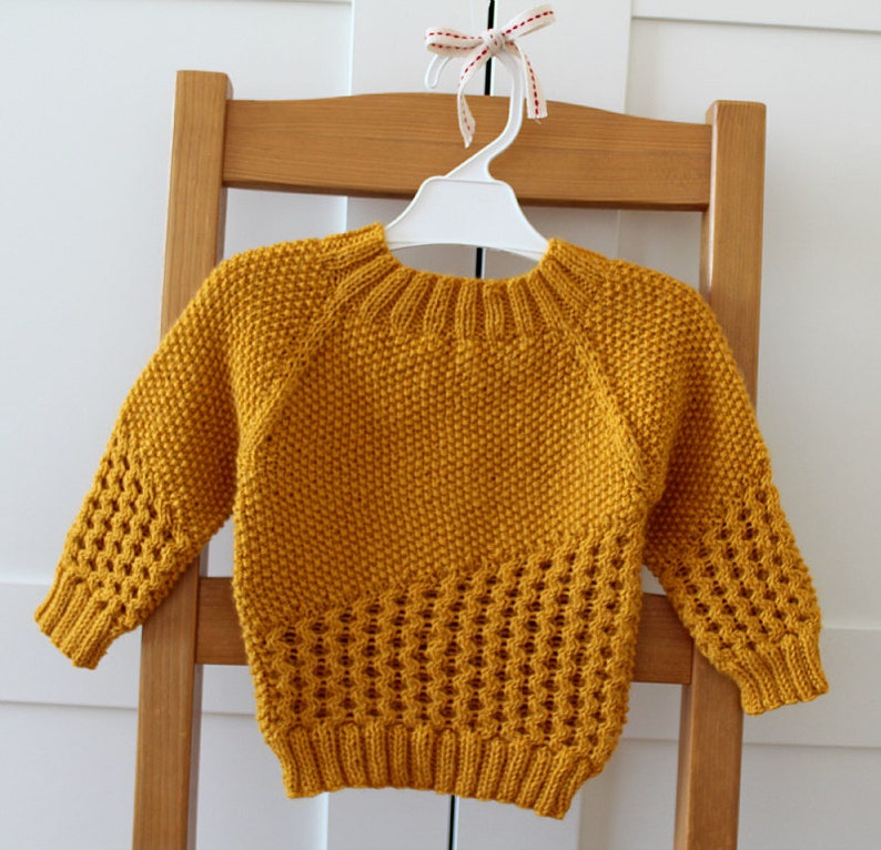 May include: A mustard yellow knitted sweater with a honeycomb stitch pattern. The sweater has a round neckline and long sleeves.