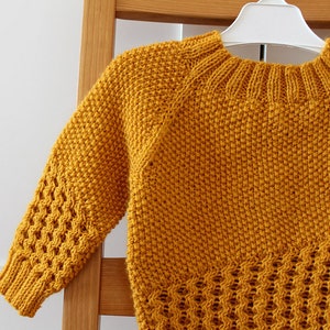 May include: A mustard yellow knitted sweater with a cable knit pattern on the sleeves and a basket weave pattern on the bottom.