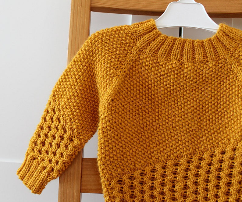 May include: A mustard yellow knitted sweater with a cable knit pattern on the sleeves and a basket weave pattern on the bottom.