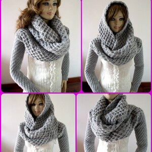 May include: Gray knitted cowl neck scarf with a hood. The scarf is made of a chunky yarn and has a waffle stitch pattern.