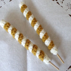 May include: Two crocheted striped cords in white and mustard yellow with wooden sticks attached to the ends.