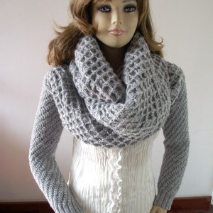 May include: A gray knitted cowl neck sweater with long sleeves. The sweater has a waffle knit texture.