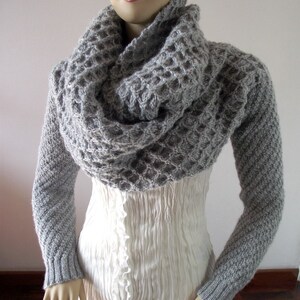 May include: A gray knitted cowl neck sweater with long sleeves. The sweater has a waffle knit texture.