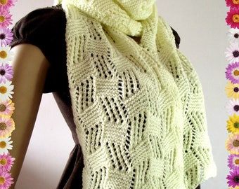May include: A light yellow knitted scarf with a lacy pattern. The scarf is draped around a person's neck and shoulders.