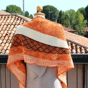 May include: A triangular shawl with a white, brown, and orange striped pattern. The shawl is made of a soft, textured yarn and has a fringed edge.