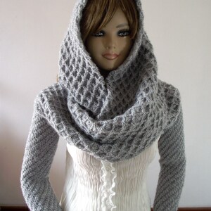 May include: A gray knitted cowl neck sweater with long sleeves and a hood. The sweater is made of a soft, textured yarn.