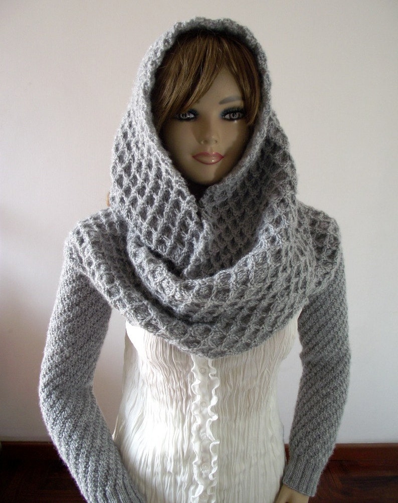 May include: A gray knitted cowl neck sweater with long sleeves and a hood. The sweater is made of a soft, textured yarn.
