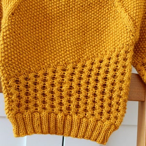 May include: A yellow knitted sweater with a textured pattern. The sweater has a loose fit and long sleeves.
