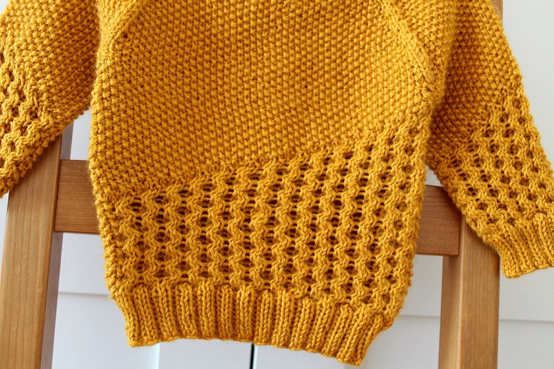 May include: A yellow knitted sweater with a textured pattern. The sweater has a loose fit and long sleeves.