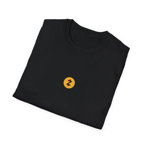 Op de afbeelding: Zwart T-shirt met een klein, geel cirkelvormig embleem met een gestileerd "N"-ontwerp. Het shirt is opgevouwen, met de ronde hals en de plaatsing van het embleem op de borst. De stof lijkt zacht en comfortabel.