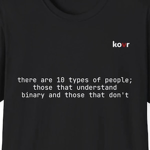 Peut inclure: T-shirt noir avec texte blanc : "Il existe 10 types de personnes ; ceux qui comprennent le binaire et ceux qui ne le comprennent pas." Le mot "kovr" est imprimé en rouge et blanc en haut à droite.