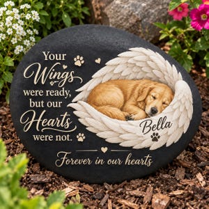 May include: A black memorial stone featuring a golden retriever puppy sleeping inside white angel wings. The text reads: Your Wings were ready, but our Hearts were not. Bella. Forever in our hearts. Includes small paw prints and heart icons.