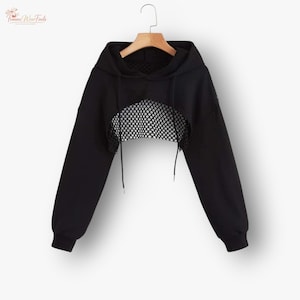 Könnte beinhalten: Schwarzer, gecroppter Hoodie mit Mesh-Einsatz auf der Brust. Der Hoodie hat lange Ärmel, eine Kapuze mit Kordelzug und eine lockere Passform. Das Mesh-Panel fügt ein einzigartiges Designelement hinzu.