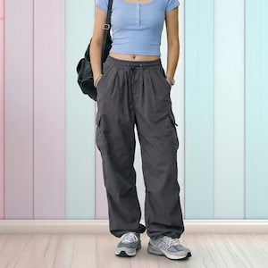 May include: A person wearing a light blue short-sleeved top and dark gray cargo pants with pockets. The person is also wearing gray sneakers with white soles and carrying a black backpack. The background is a colorful vertical striped wall.