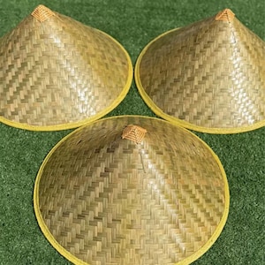 May include: Three conical hats crafted from woven light brown bamboo strips. Each hat features a pointed top with a small square woven accent and a circular brim finished with a smooth, light yellow border trim along the outer edge.