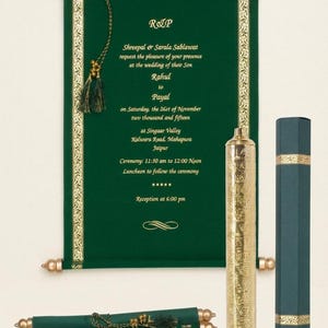 Puede incluir: Invitación de boda verde esmeralda con detalles dorados. El texto está en una fuente formal. Incluye un estuche dorado, una caja verde oscuro y una invitación enrollada más pequeña.