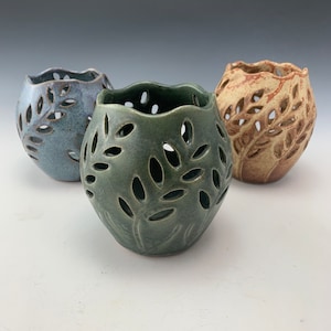 May include: Three ceramic candle holders with a leafy design. The candle holders are in shades of blue, green, and brown.
